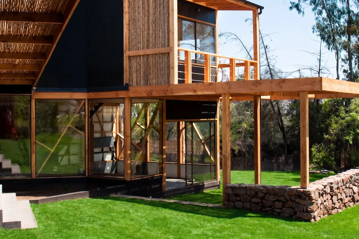 Casa Minillas en Santiago: volumen de madera y vidrio sobre pilares, con muro de piedra, obra de CCP Arquitectura